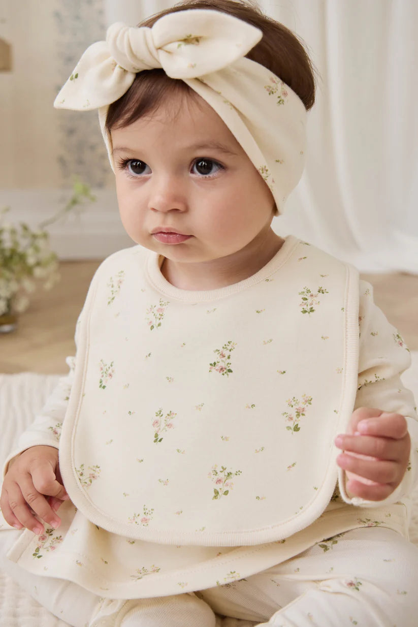 Baby wearing a floral bib and headband in a soft, neutral setting