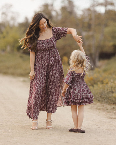 This picture depicts a mother and daughter dancing in matching dresses. this shows the little girl modeling the dress from the back. 