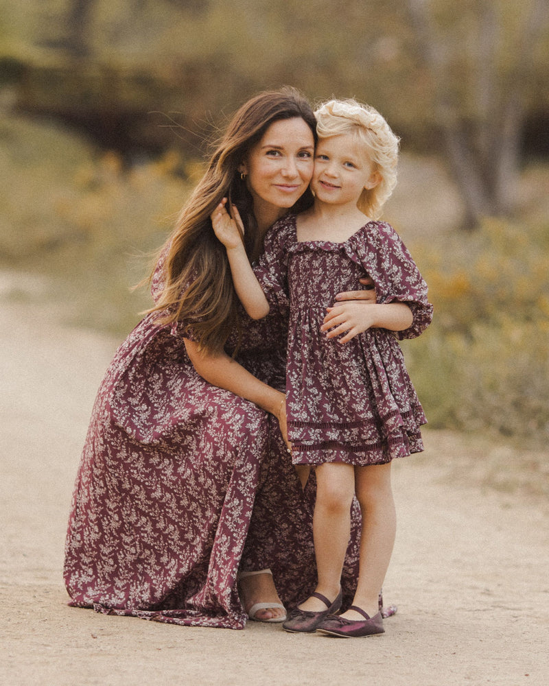 This picture shows the mother daughter modeling matching dresses. each dress is a wine color with florals all over the dress. 