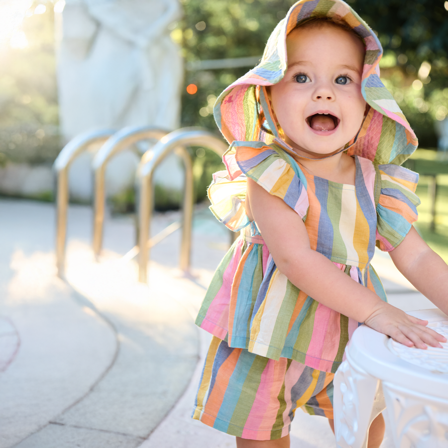 Child wearing a colorful striped dress and sun hat outdoors