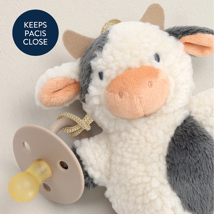Plush cow toy with a pacifier attached on a light beige background