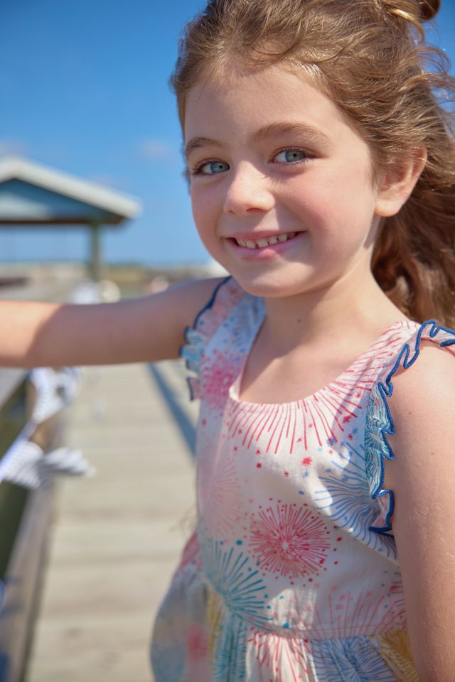Young girl in a colorful dress standing on a wooden boardwalk with a clear blue sky.