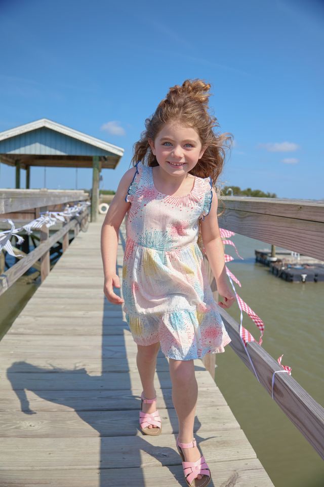 Young girl in a colorful dress standing on a wooden dock by a body of water.