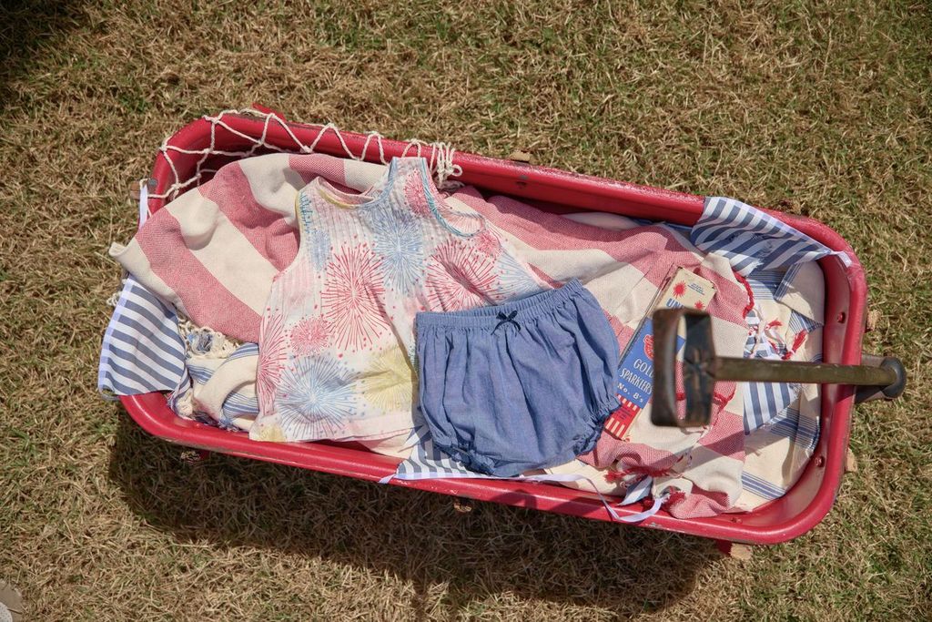 Children's clothing in a red toy wagon on grass