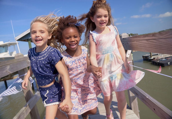 Three young girls holding hands on a dock with boats in the background