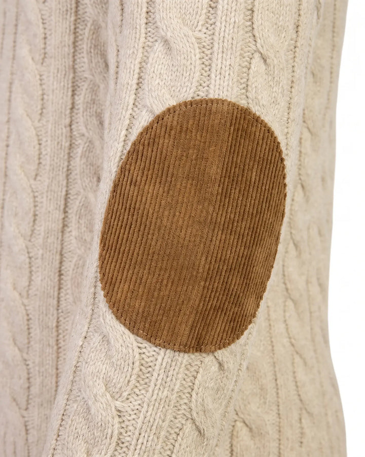 Close-up of a cream cable-knit sweater with a brown oval corduroy elbow patch on the front.