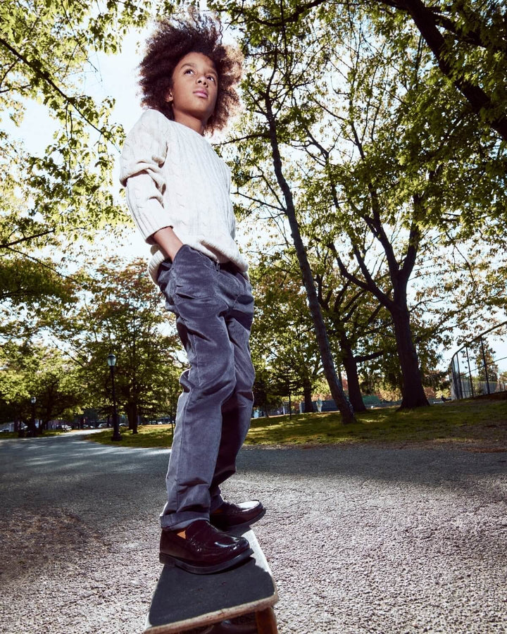 Child standing on a skateboard in a park with trees and grass in the background