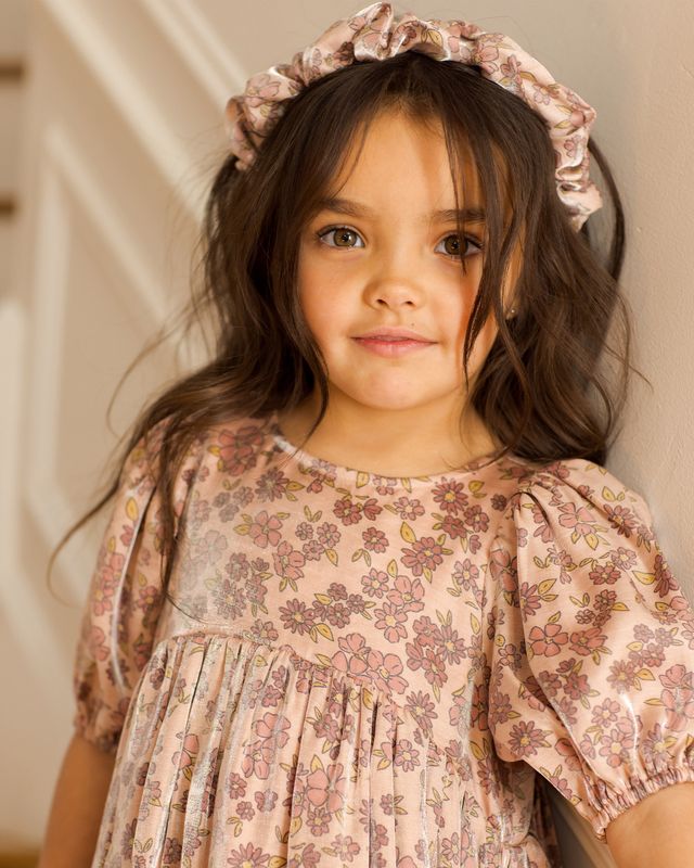 Young girl wearing a floral dress and headband against a neutral background