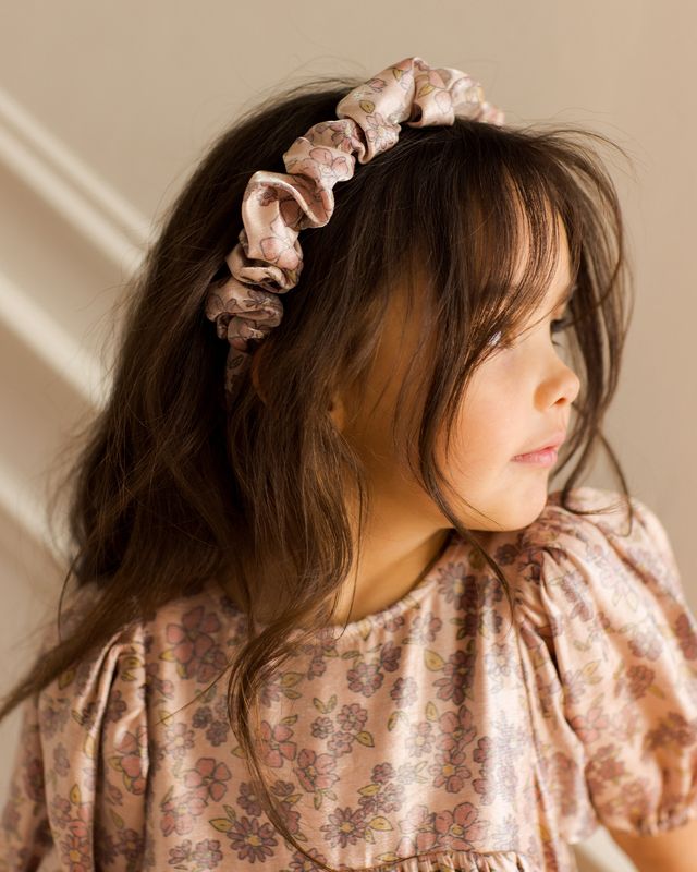 Child wearing a floral headband and dress against a neutral background