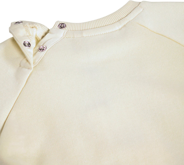 Close-up of a cream-colored long-sleeve top with a ribbed crew neck and three silver snap buttons on the shoulder.