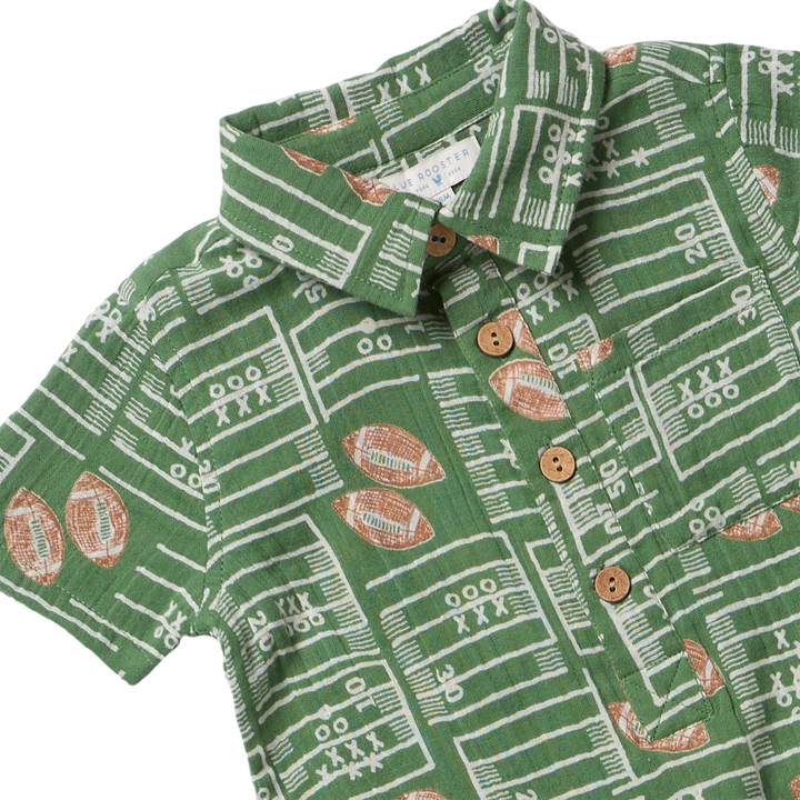 A close-up of a green short-sleeve collared shirt with a white football field line pattern and brown football motifs, featuring three brown buttons on the front.