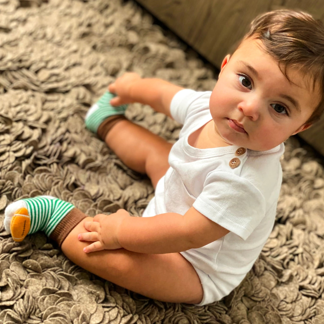 baby wearing striped socks with tiny footballs on the toes. 