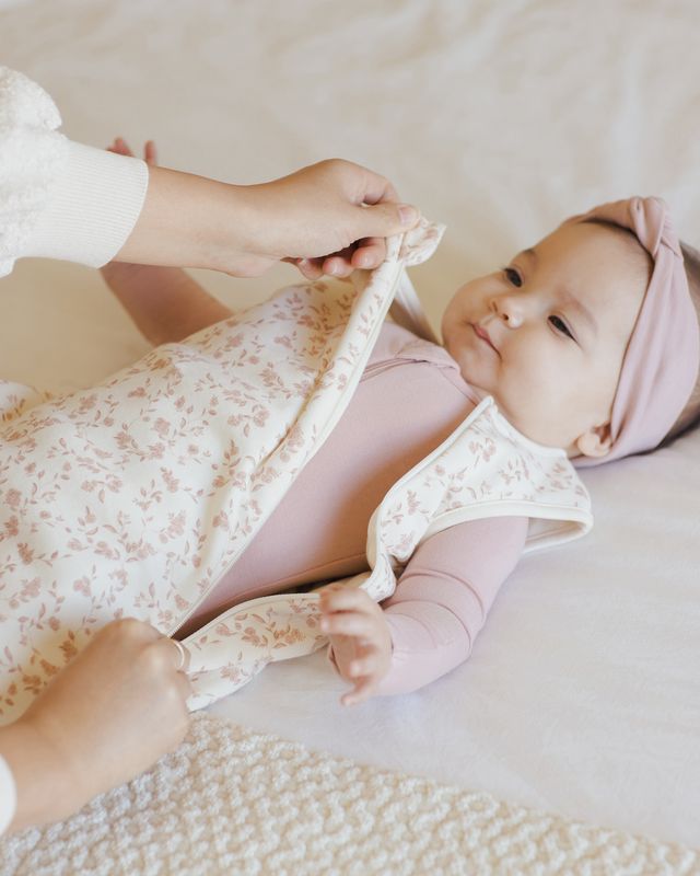 Baby in pink sleep sack with floral blanket print. this shows the sleep sack being unzipped 