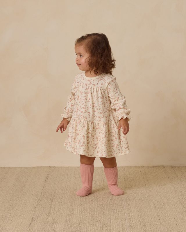 Young child wearing a floral dress and pink socks on a beige background