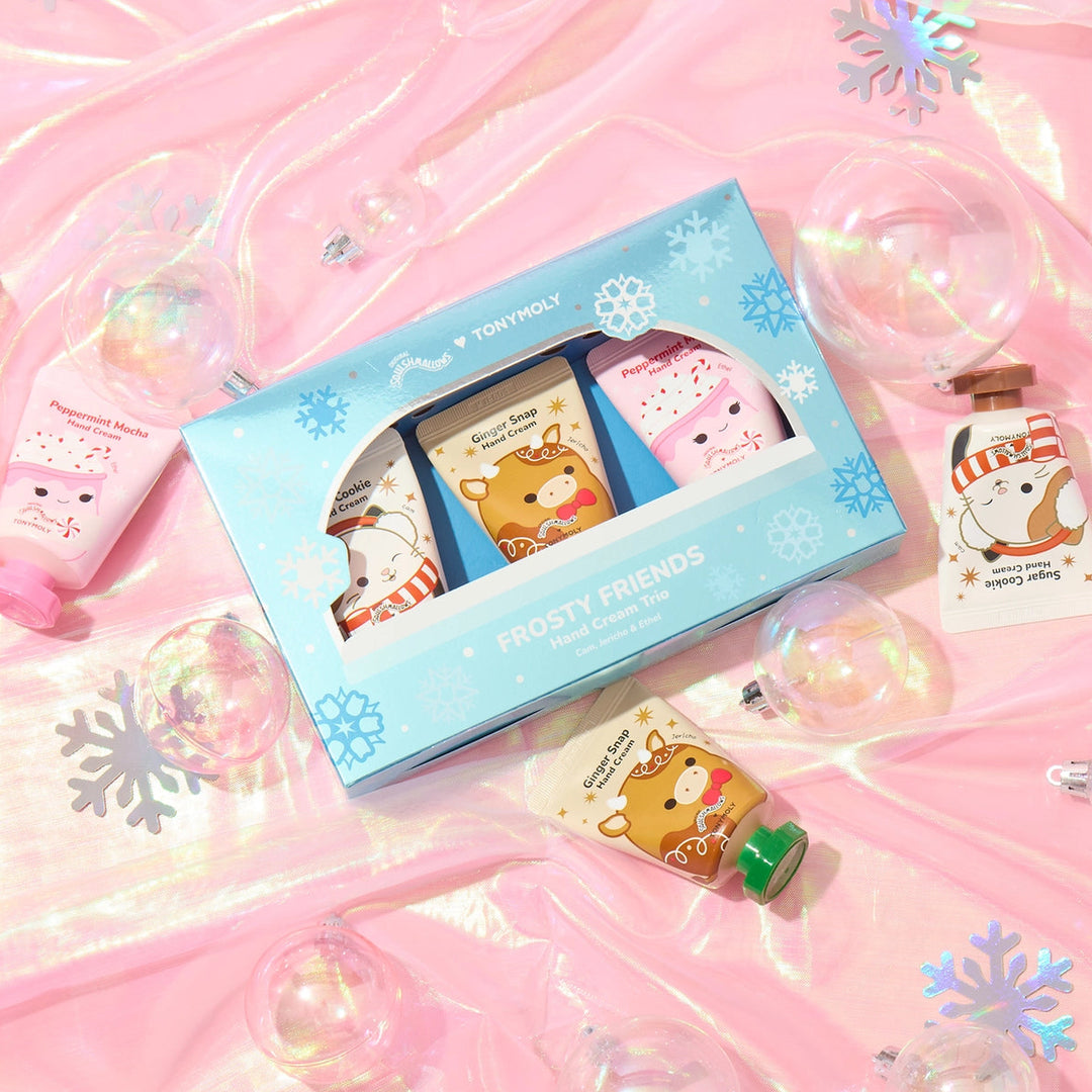 A pink-themed hand cream and hand cream set gift box by TONYMOLY, styled on a shiny pink background with iridescent ornaments. The set includes a light blue box with cartoon bear illustrations, a pink hand cream tube, and a small hand cream tube with a green cap.