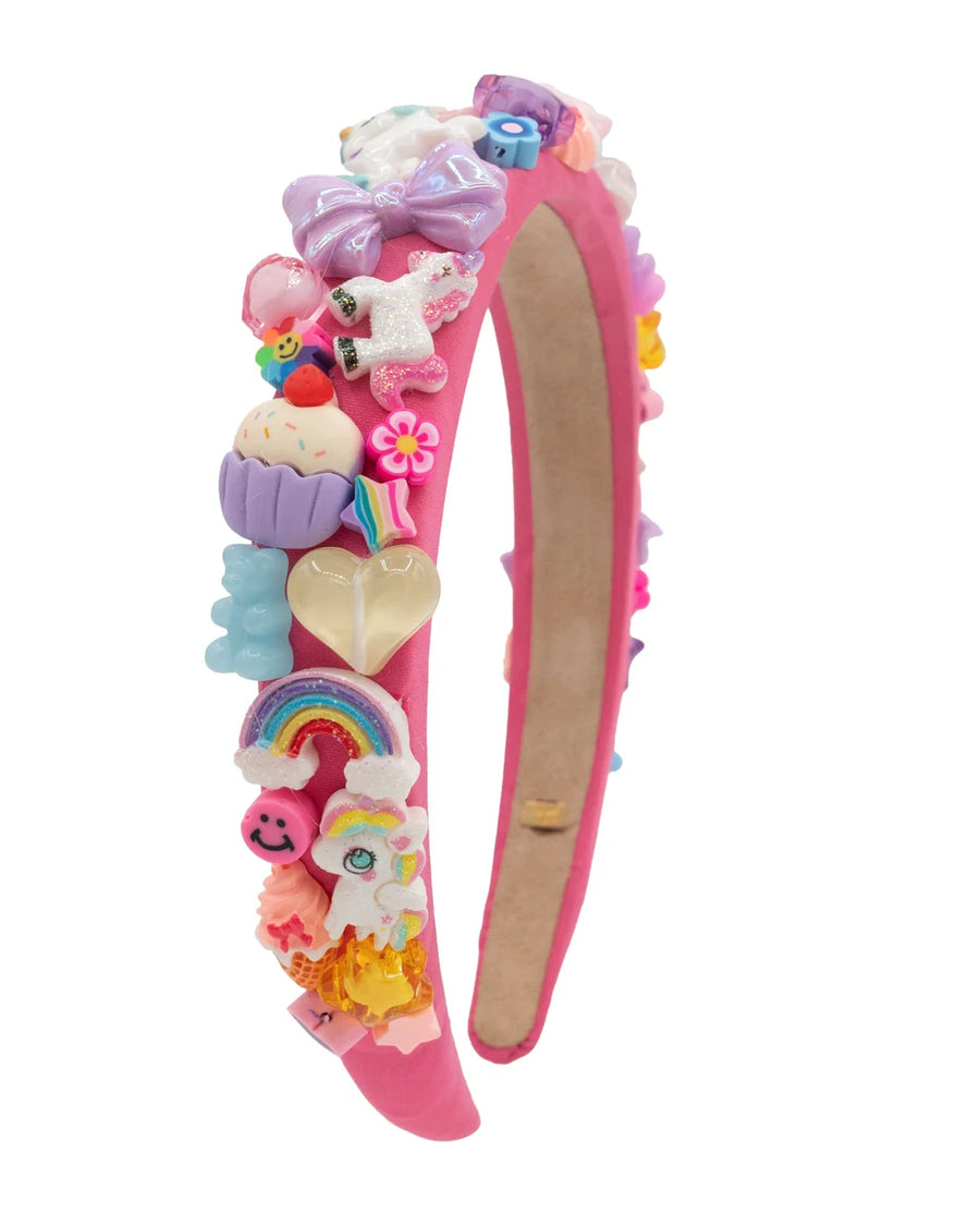 A pink headband decorated with various colorful, whimsical charms including unicorns, cupcakes, a rainbow, a heart, and a pink bunny, shown on a plain white background.