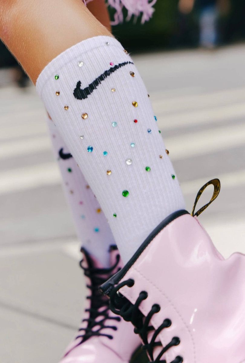 White Nike crew socks embellished with rhinestones and a black swoosh, worn with light pink boots.