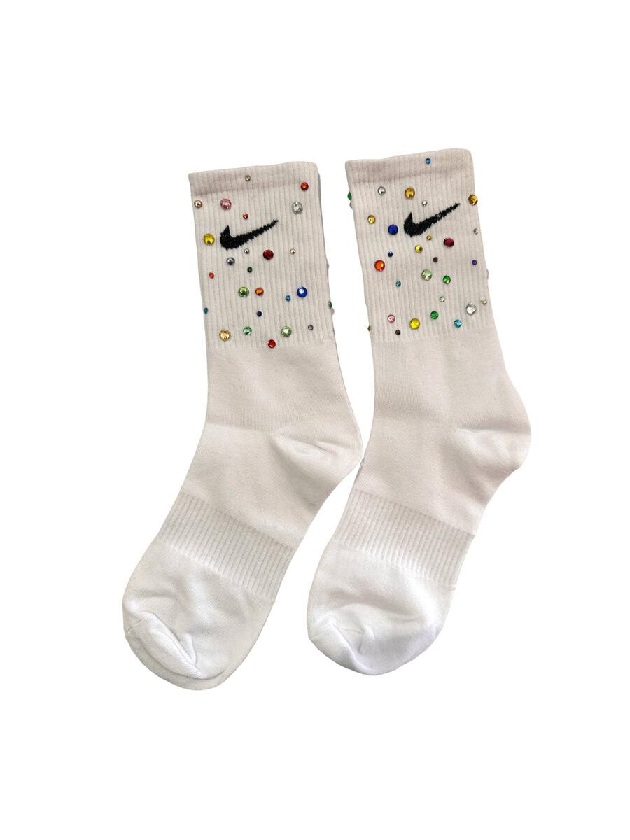 A pair of off-white Nike crew socks decorated with colorful rhinestones and a black Swoosh logo on the upper cuff, shown against a plain white background.