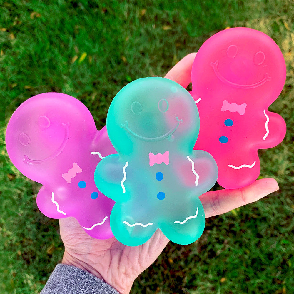 Three colorful gingerbread man-shaped toys held in a hand against a grass background