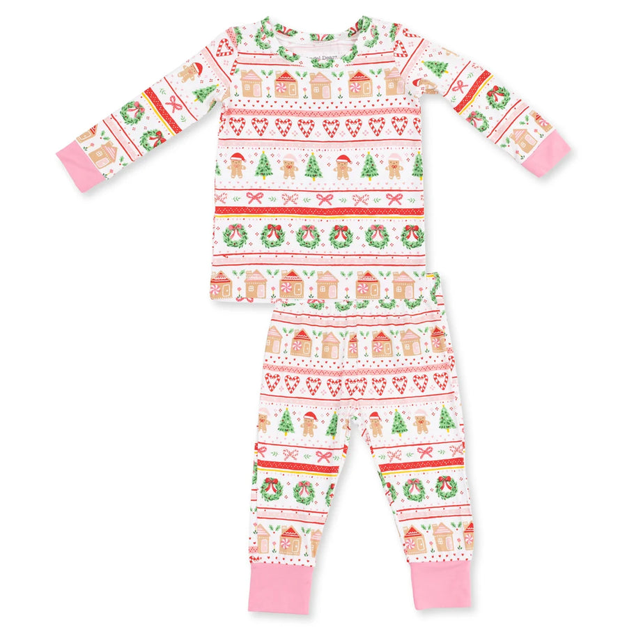 A two-piece baby pajama set featuring a long-sleeve top and matching pants with a festive Christmas fairytale print. The print includes gingerbread houses, Christmas trees, snowman motifs, and wreaths in red, green, and beige on a white background, finished with solid pink cuffs and ankles.