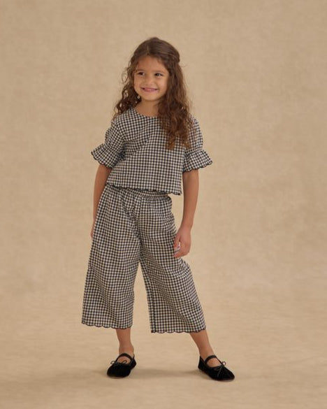 Young girl wearing a black and ivory gingam checkered outfit on a beige background
