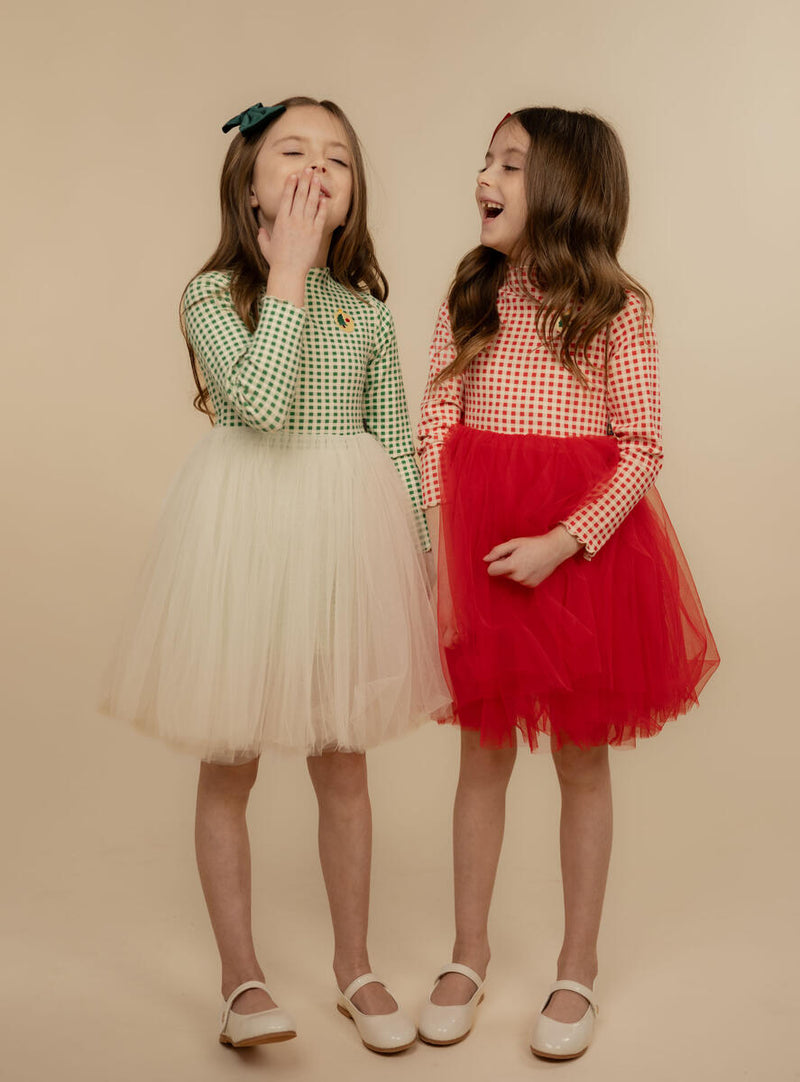 two little girls modeling the holiday tulle dresses, one in green and white and one in red and white. 