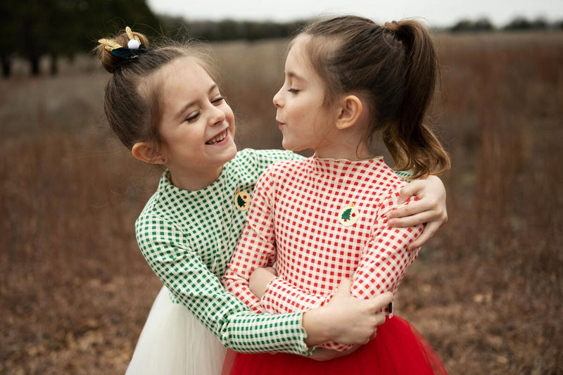 two little girls modeling the holiday dresses. one girl in red and white and the other in green and white gingham. 