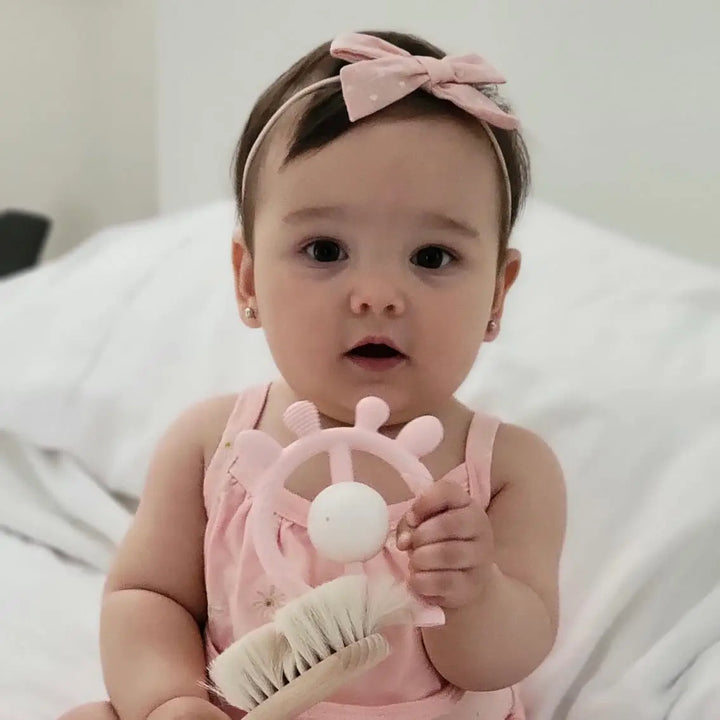 Baby in pink outfit holding a teething toy with a white background