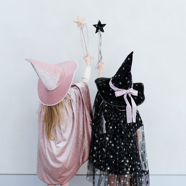 Two children in witch costumes with pink and black hats against a white background