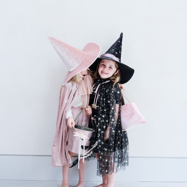 Two children in witch costumes with pink and black hats against a white background