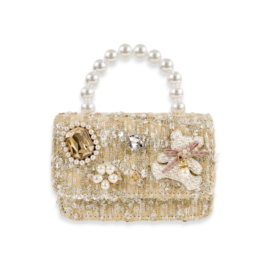 A miniature structured tweed handbag in beige and gold, embellished with faux pearls, crystals, and floral appliqués, featuring a pearl-beaded top handle on a white background.