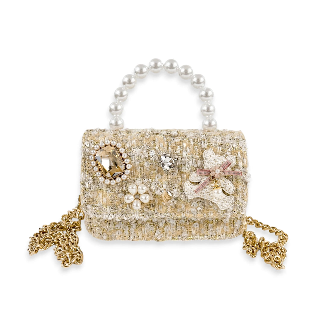 A small structured handbag with a pearl handle, textured beige and gold tweed body, embellished with rhinestones, floral appliqué, and gold chain straps on a white background.