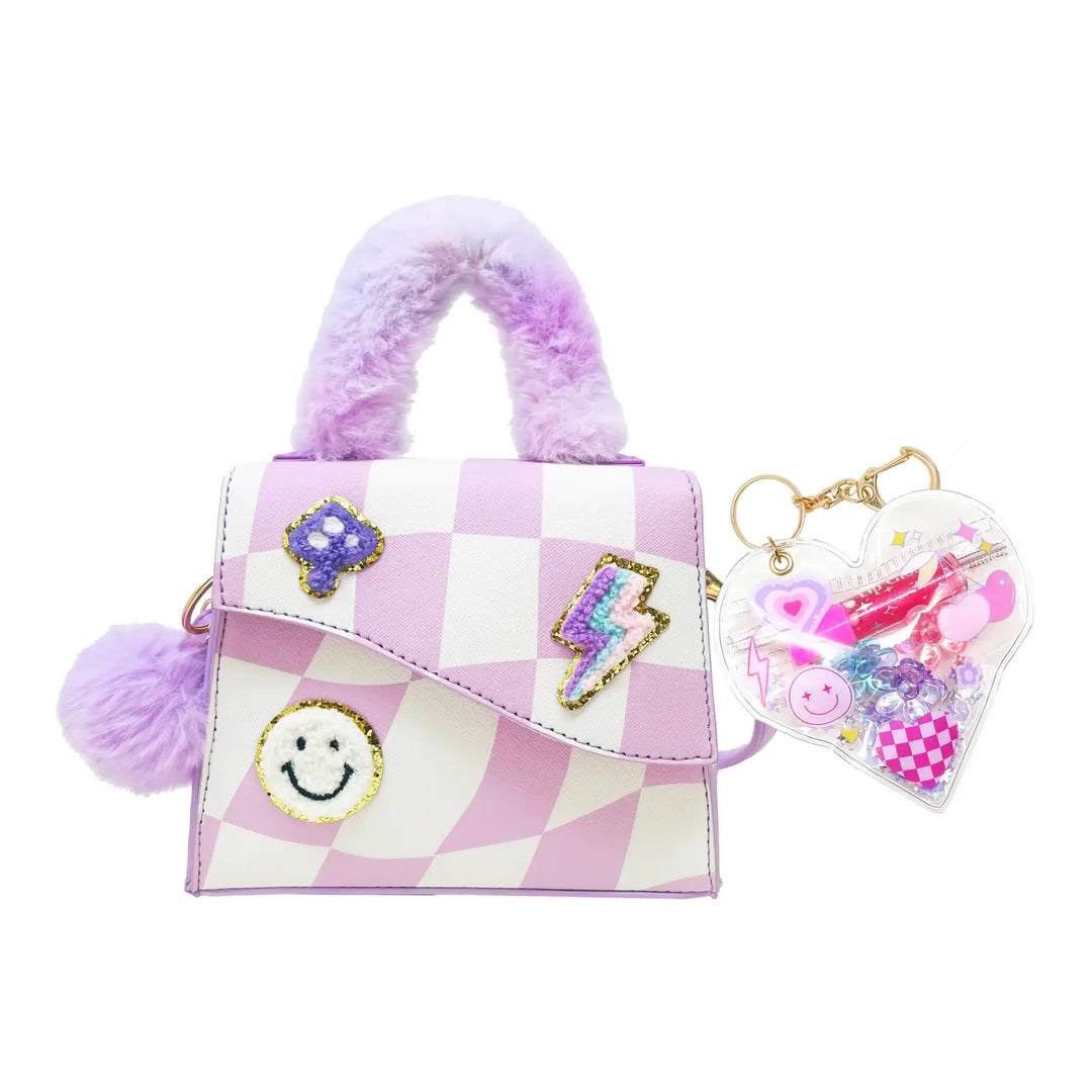 A purple and white checkered mini handbag with fuzzy lavender handles, decorated with a smiley face patch, a lightning bolt patch, and a purple flower patch. It features a matching fuzzy pom-pom handle and a heart-shaped keychain filled with colorful glitter and charms.
