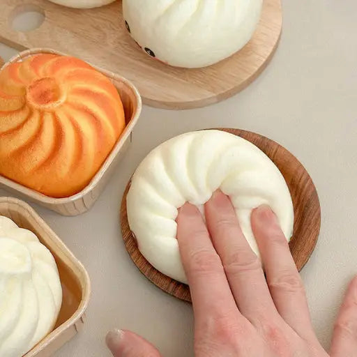 Hand holding a white steamed bun on a wooden plate with other buns in the background.