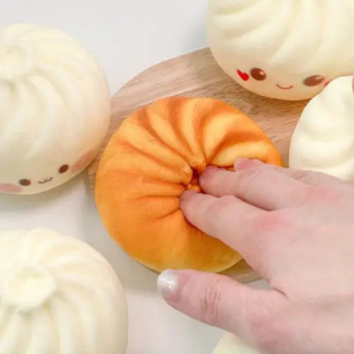 Hand interacting with a plush toy resembling a bun on a wooden board.
