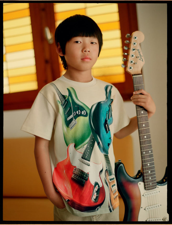 Child holding a guitar with a colorful t-shirt featuring guitar designs.