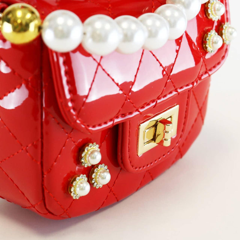 side view of the red patent leather purse. pearl handle and gold hardware. small pearls attached the bag and flap on the bag