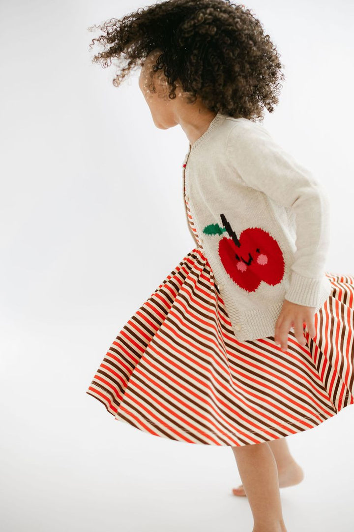 Child wearing a white sweater with a red apple design and a red and orange striped skirt on a white background