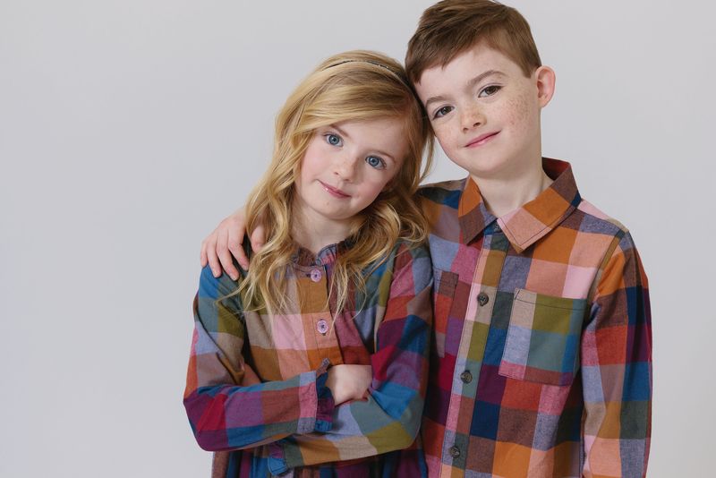 Two children wearing colorful checkered shirts against a plain background