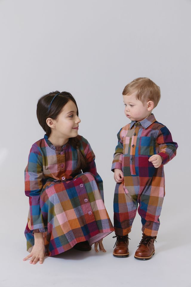 Two children in matching plaid outfits on a white background
