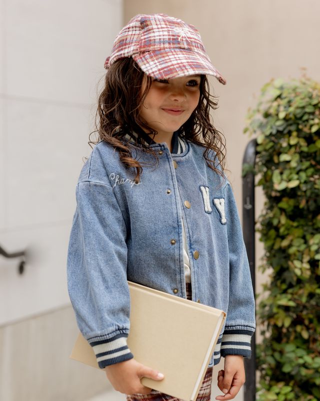 Child wearing a blue denim jacket and plaid cap, holding a beige folder.