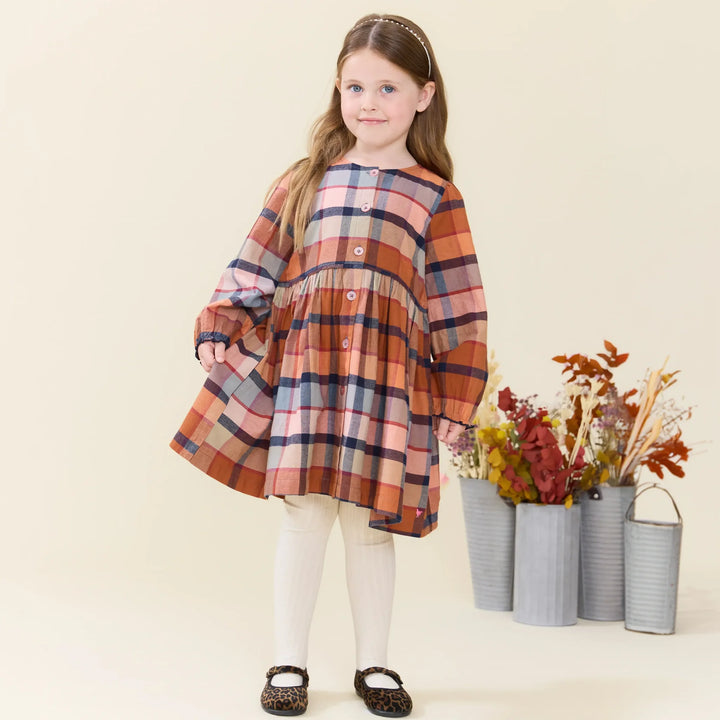 young girl wearing rust plaid dress with long sleeves and buttons down the center. 