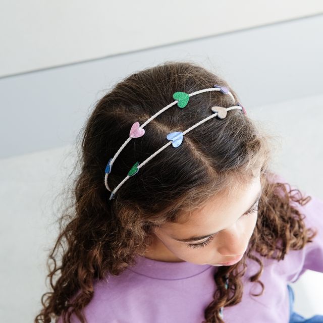 Child wearing a headband with colorful heart-shaped clips on a plain background