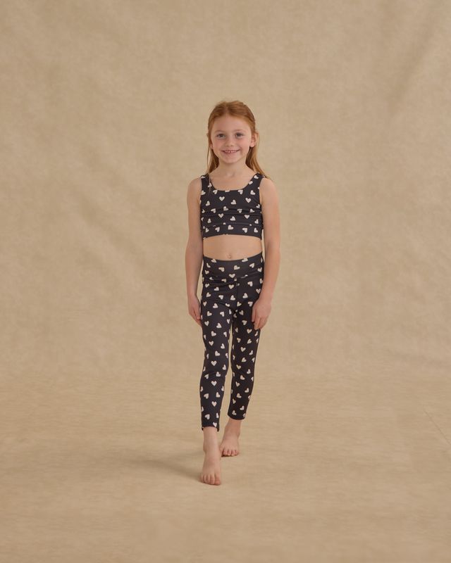 Young girl wearing a matching heart patterned top and leggings set on a beige background