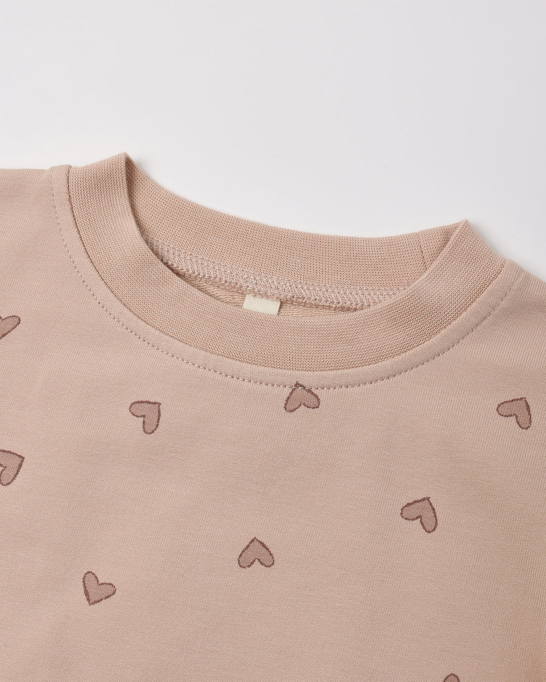 Close-up of a crewneck sweatshirt in a dusty rose pink color, featuring a small heart pattern scattered across the front.