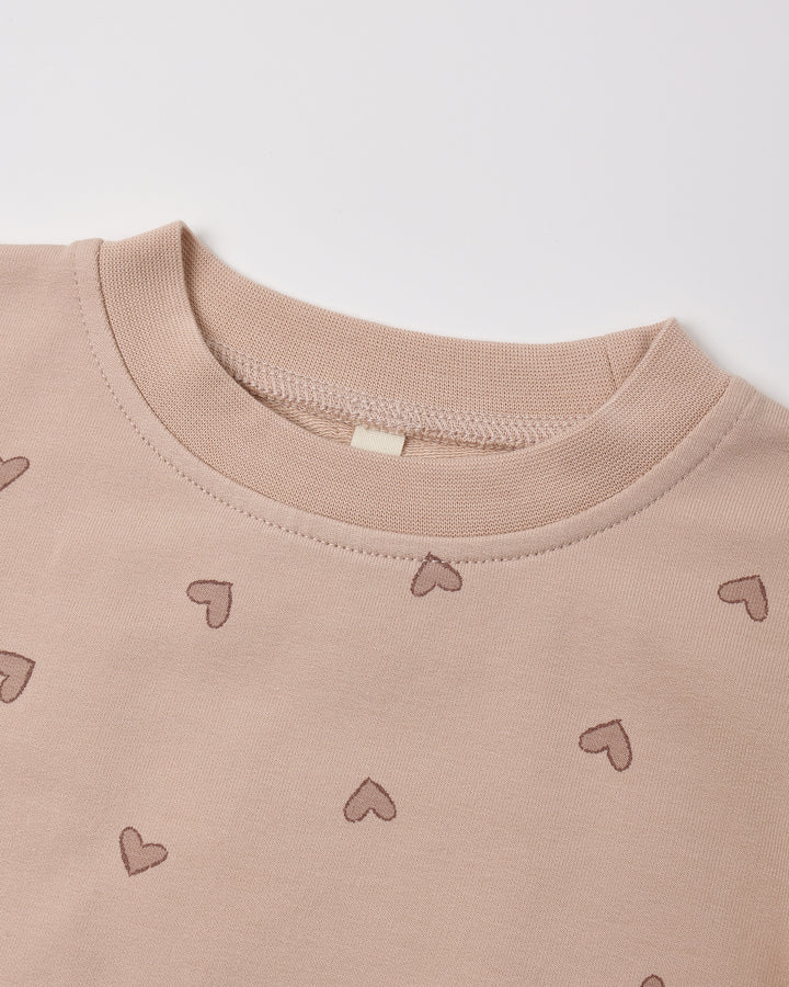 Close-up of a crewneck sweatshirt in a dusty rose pink color, featuring a small heart pattern scattered across the front.