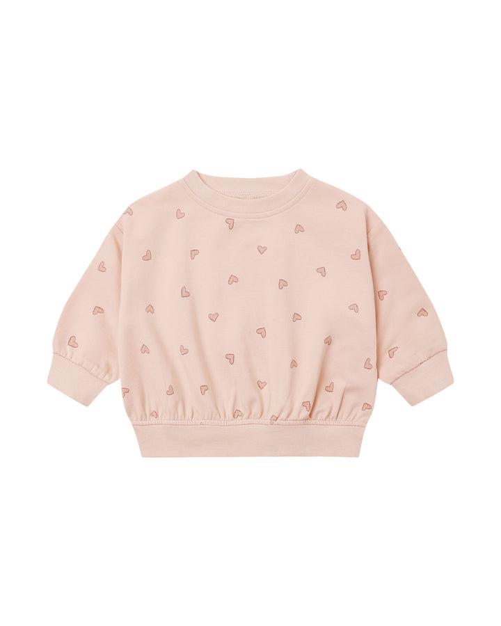 A light pink long-sleeve sweatshirt for toddlers, featuring a delicate all-over pattern of small pink hearts and a gathered elastic hem, displayed on a clean white background.