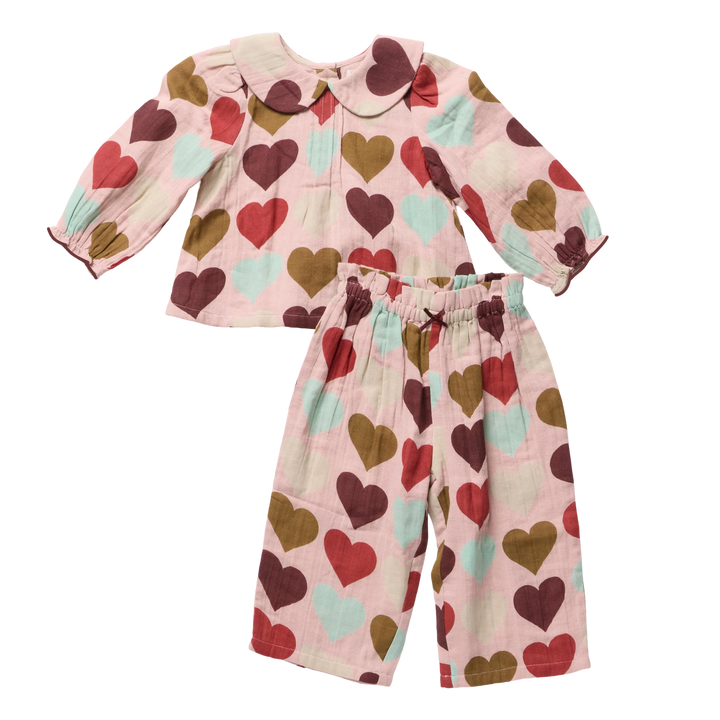 A two-piece baby outfit set featuring a long-sleeve top and matching pants in a light pink muslin fabric with a heart pattern in red, brown, and mint green, displayed on a clean white background.