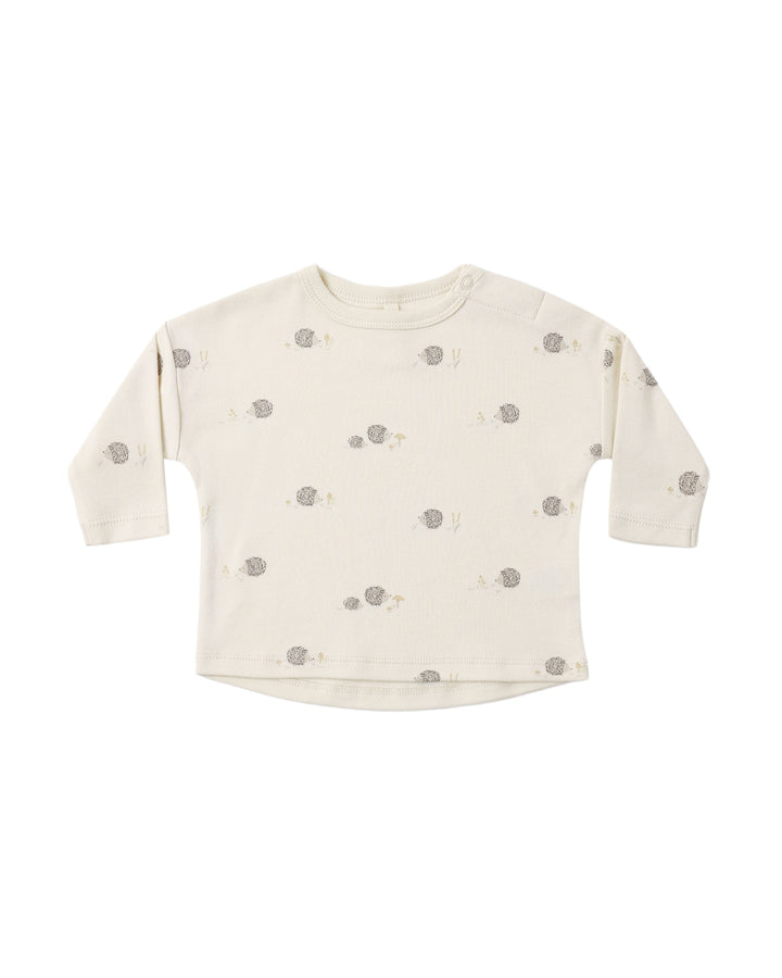 An off-white long-sleeve baby top with a small all-over print of gray hedgehogs and tiny yellow accents, displayed flat against a solid white background.