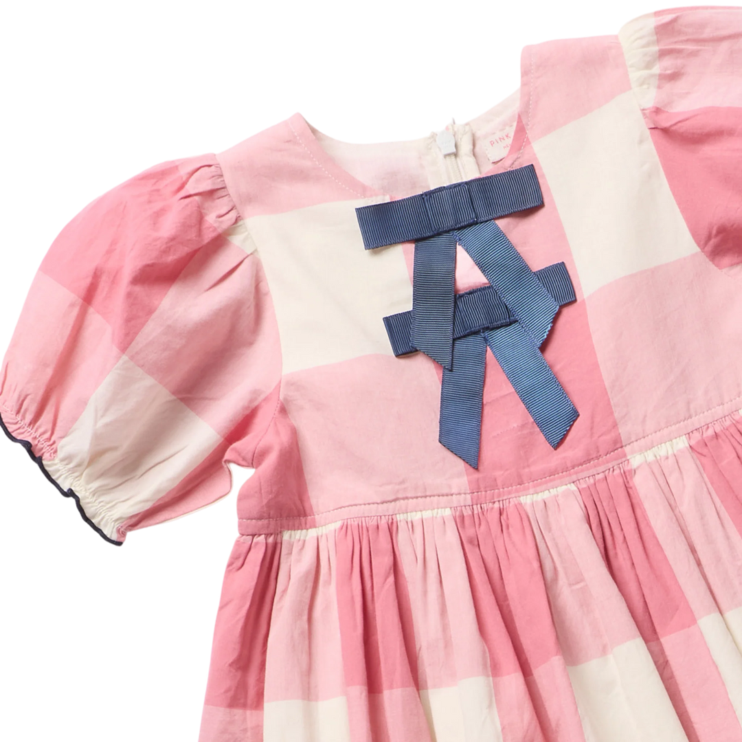 Pink and off-white checkered baby dress with a large blue ribbon bow on the chest, featuring puffed short sleeves and a gathered skirt.
